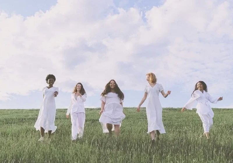 Women dressed in white clothing walking happily on grass in celebration of International Women's Day