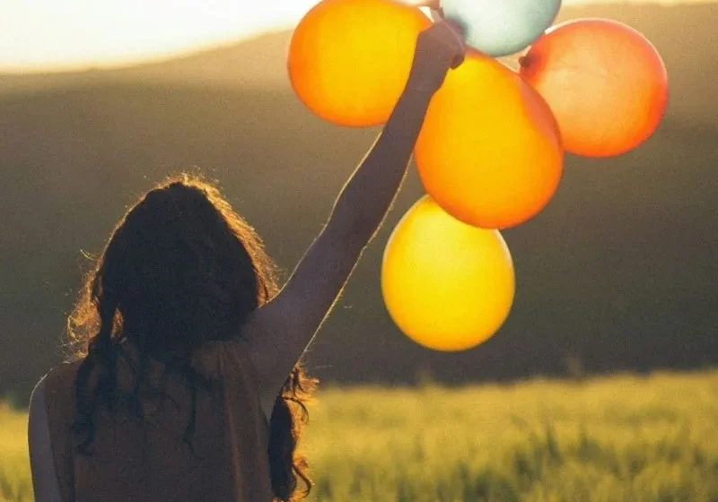 woman holding balloons in a grass field