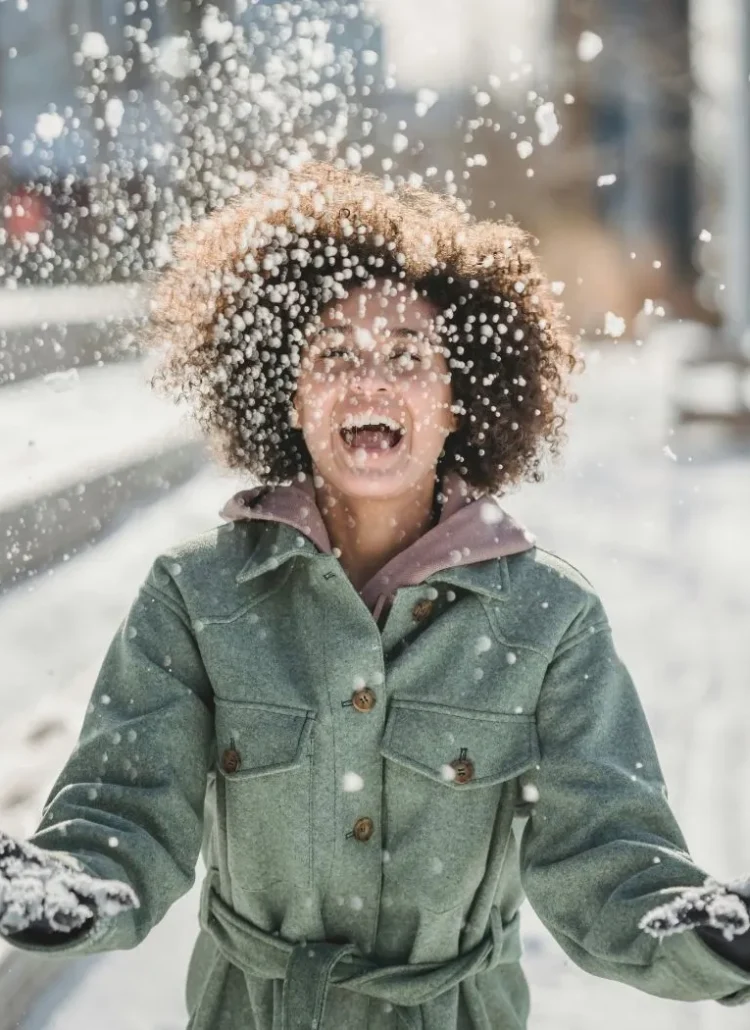 woman with big smile on her face in winter jacket throwing snow in the air