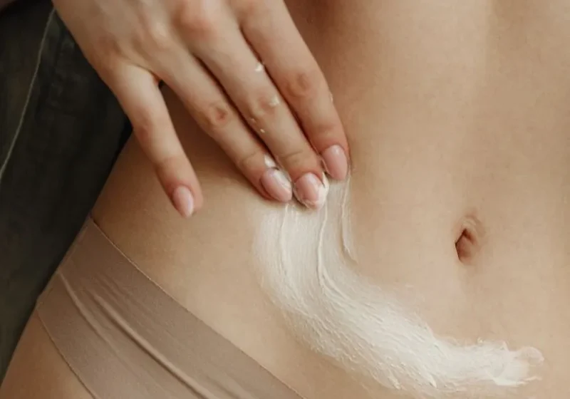 woman practicing her self-care routine, applying cream on her belly