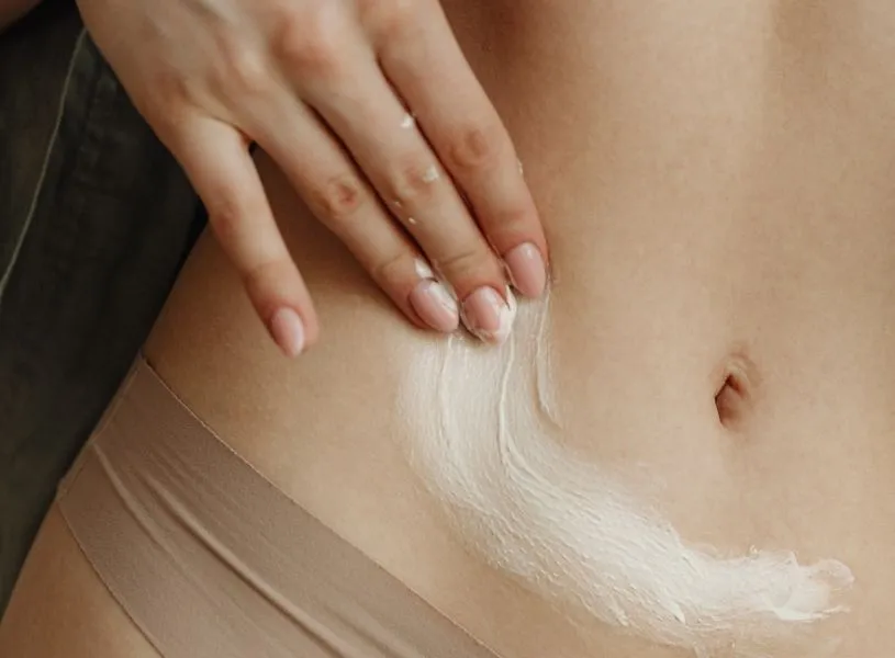 woman practicing her self-care routine, applying cream on her belly