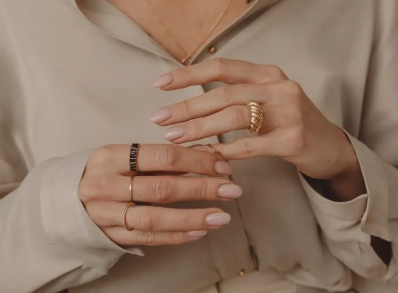 woman in beige shirt wearing rings on her fingers and have nude color nails