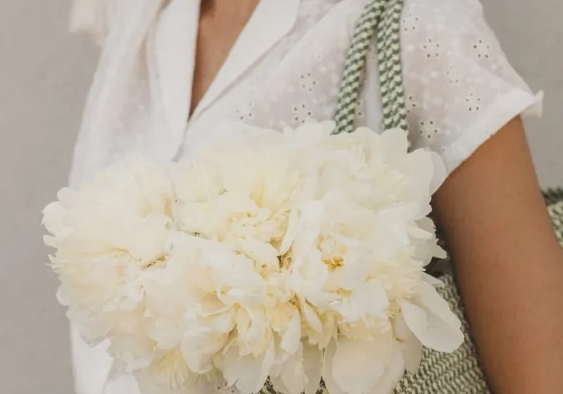 woman in white top and denim jeans wearing a bag filled with white flowers