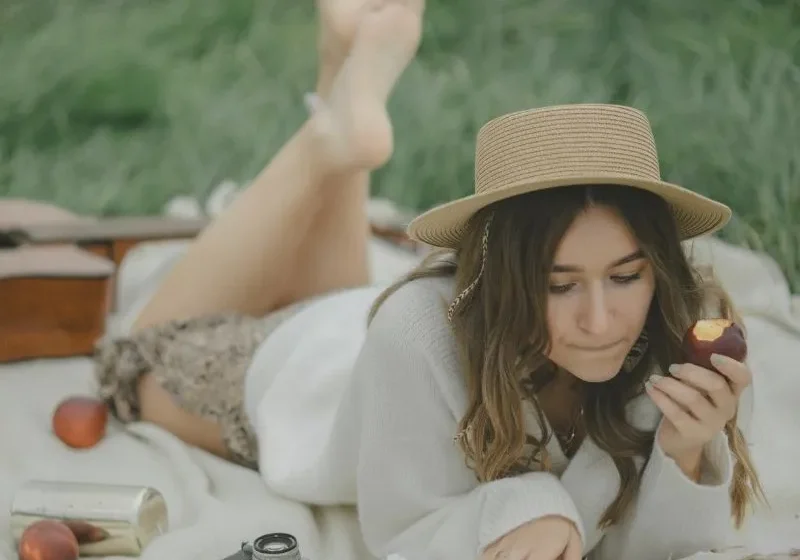 woman enjoying a solo summer picnic snacking on a fruit and reading a book