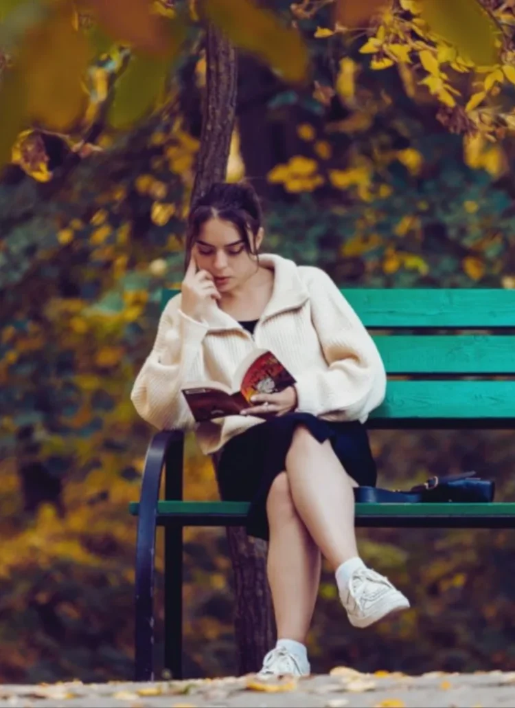 Woman doing fall solo activities. She's reading by herself at the park