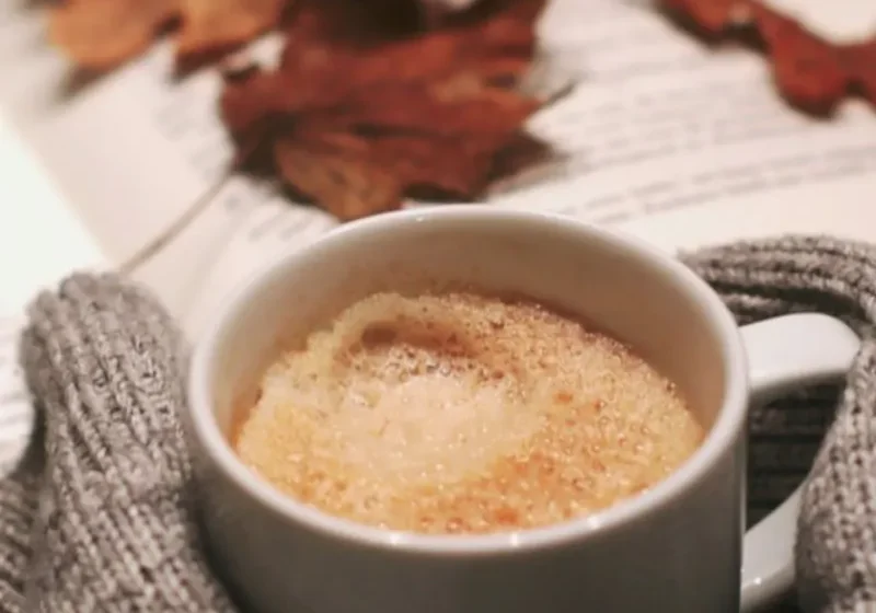 a cup of coffee with a book and fall leaves in the background