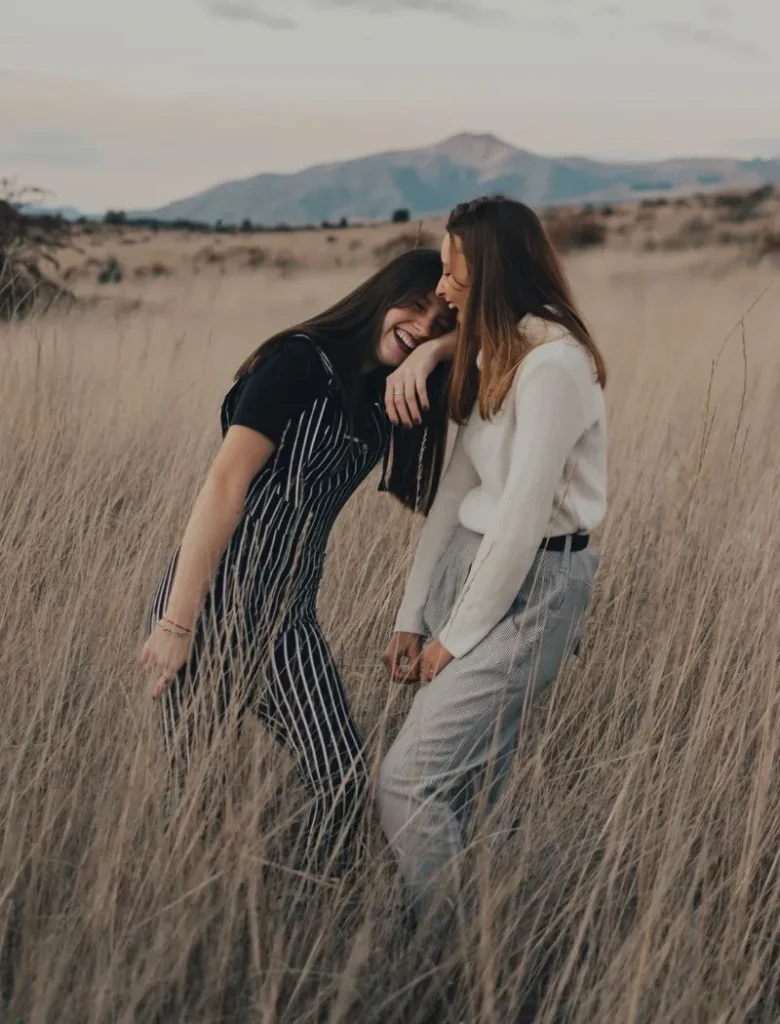 two girl friends laughing in the middle of a field