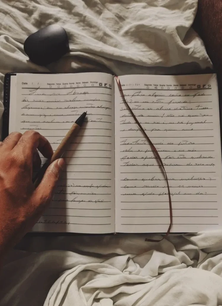 a hand holding a pen on top of a journal book