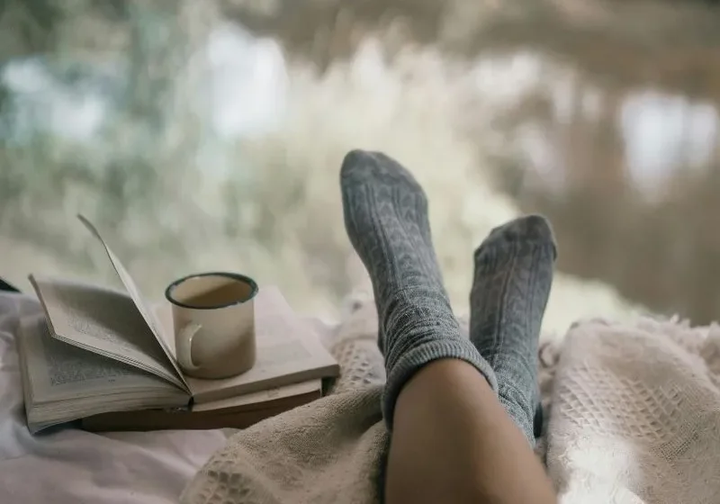 woman enjoying her solo moment. She's laying with socks on her feet and a cup of drink sitting on top of a book