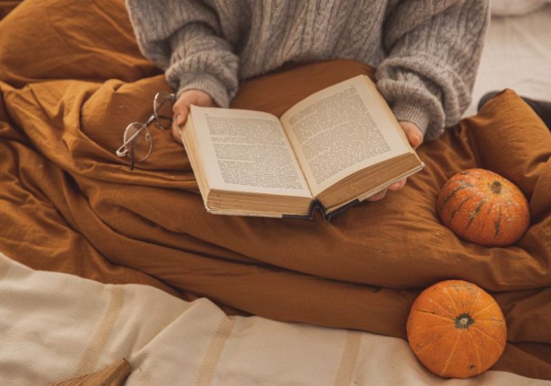 a person sitting down with a book and some pumpkins around them