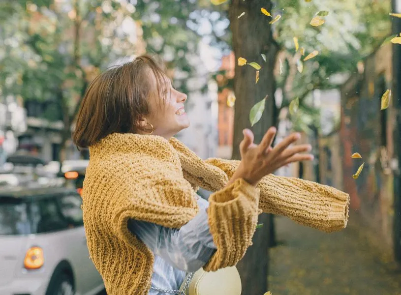 woman enjoying her best self throwing fall leaves