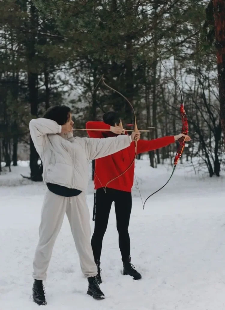 two woman standing in the snow doing archery