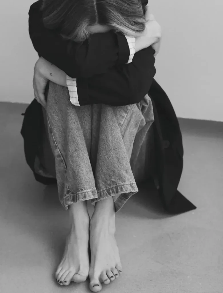 woman sitting on the floor hugging her knees with her head down