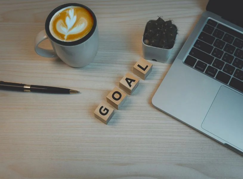 letters that spells the word goal, with coffee, notebook, and pen on table