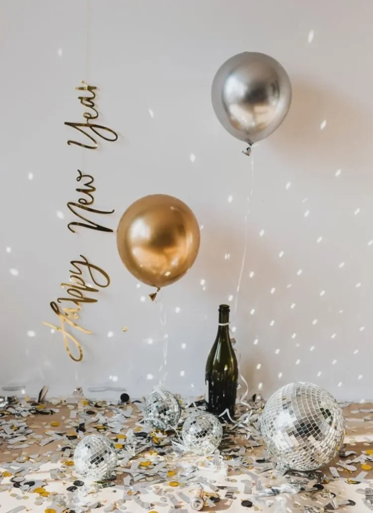 happy new year with gold and silver balloons, bottled champagne, confetti, disco ball and sparkles