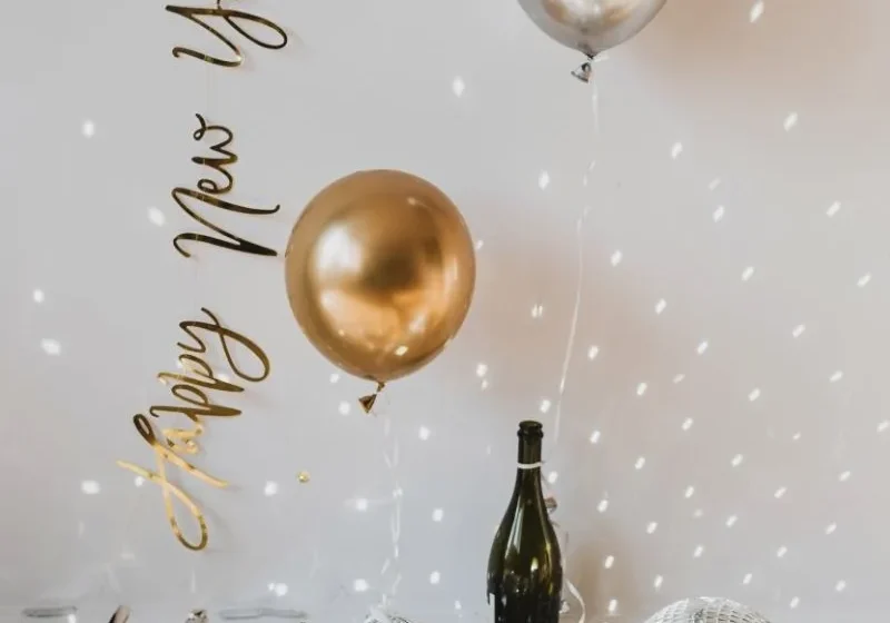 happy new year with gold and silver balloons, bottled champagne, confetti, disco ball and sparkles
