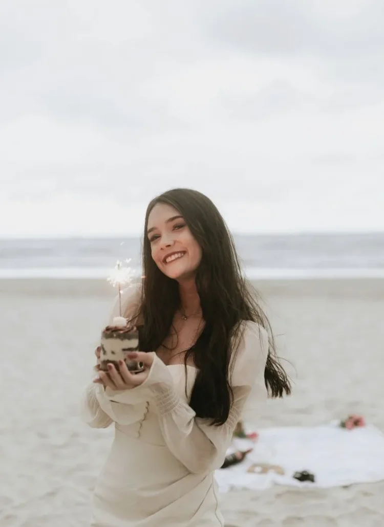 a smiling girl holding a birthday cake at the beach