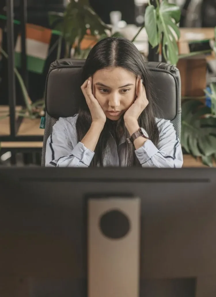 woman sitting in front of computer with hands on side of face looking stressed and frustrated