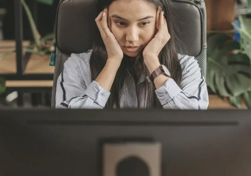 woman sitting in front of computer with hands on side of face looking stressed and frustrated
