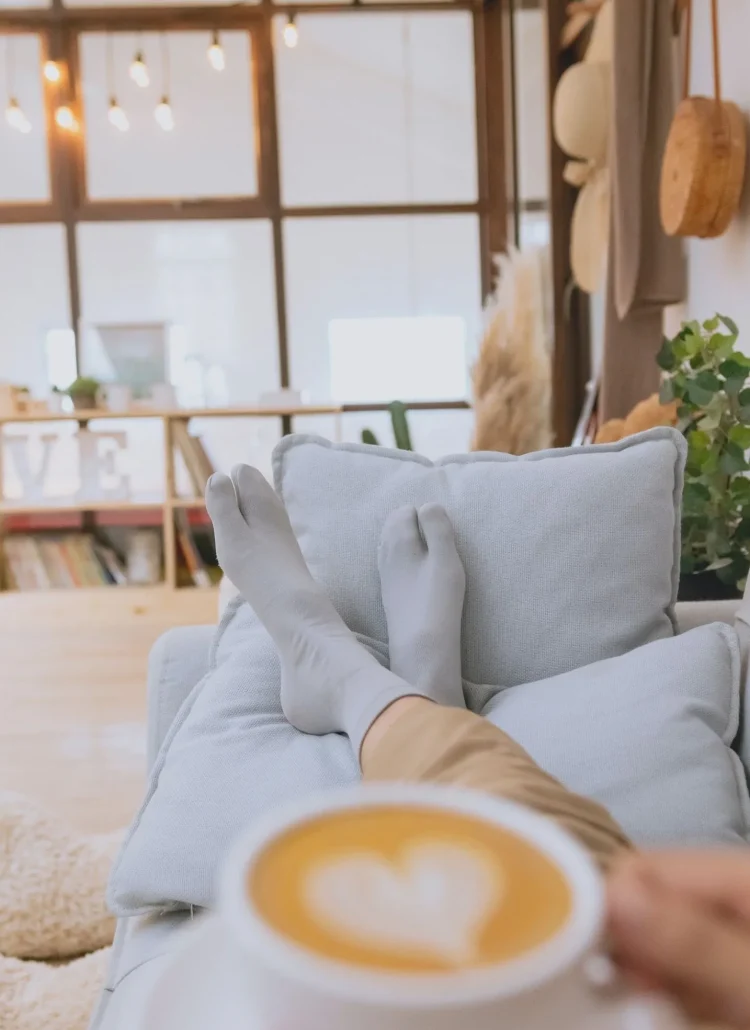 women with coffee in hand lounging on sofa with socks and in comfy environment