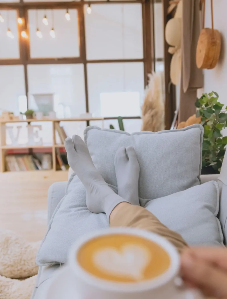 women with coffee in hand lounging on sofa with socks and in comfy environment