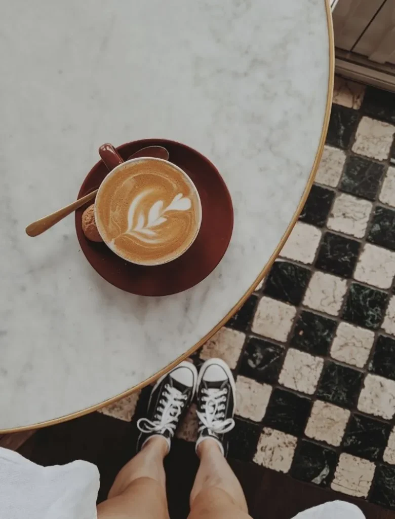 woman standing on checkerboard tiles with a coffee on the table