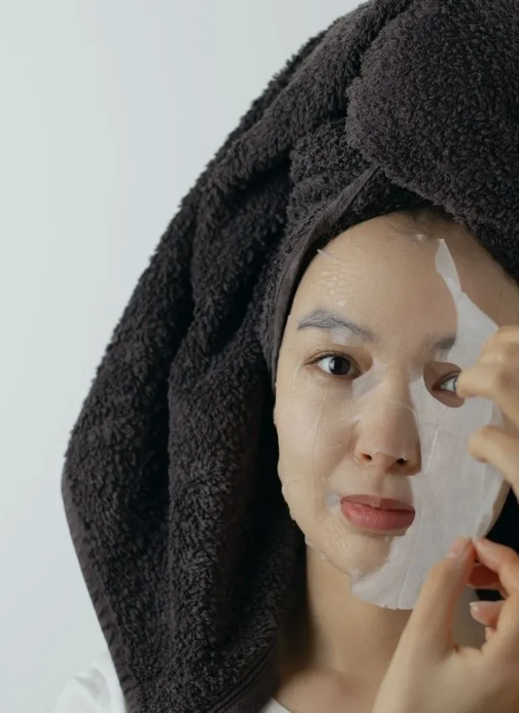 woman with towel wrapped around her head taking off a facial mask