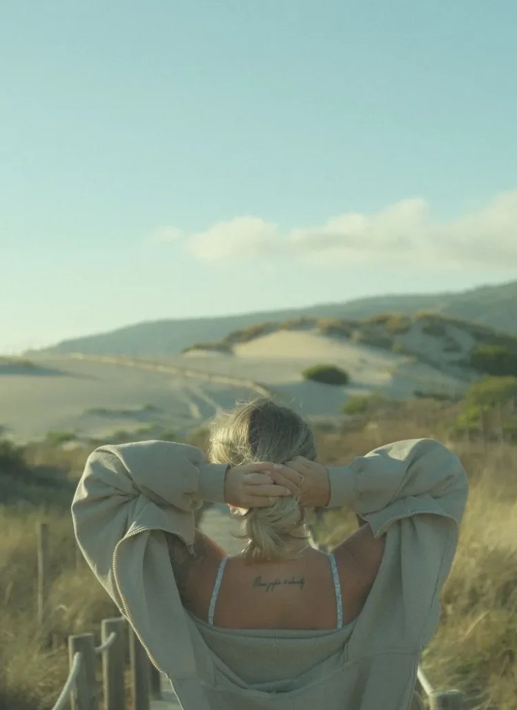 woman with hand behind her head looking out into the horizon/field