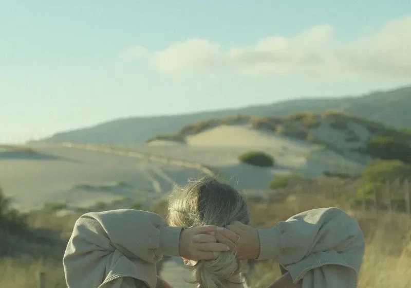 woman with hand behind her head looking out into the horizon/field