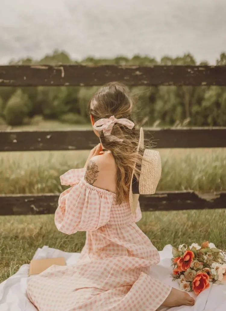 woman having a solo picnic in checkered pink and white dress looking out to the horizon