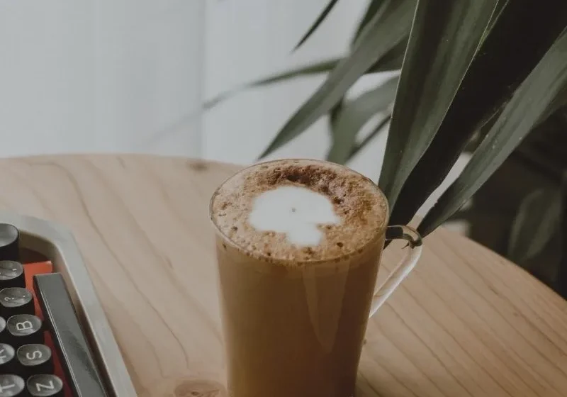 coffee, laptop and book on a table with a plant in the background