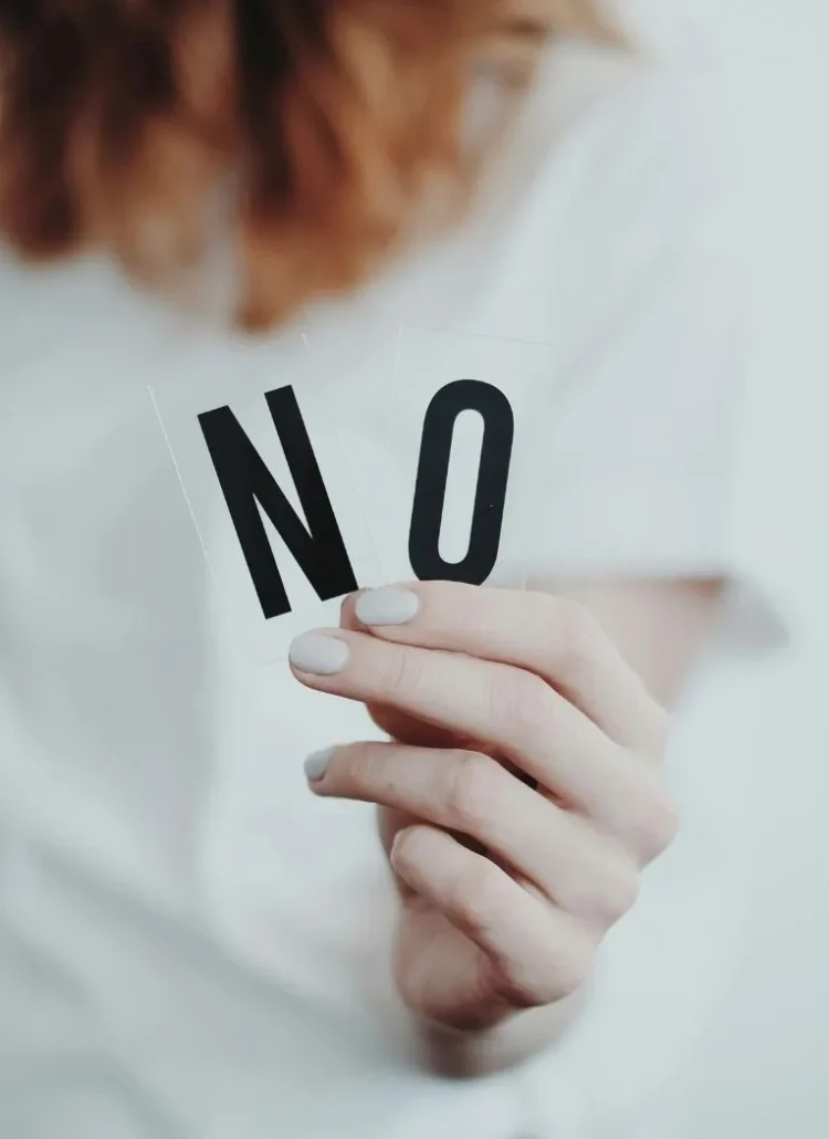 a women in white top with red hair holding "No" in her hand as a sign of rejection