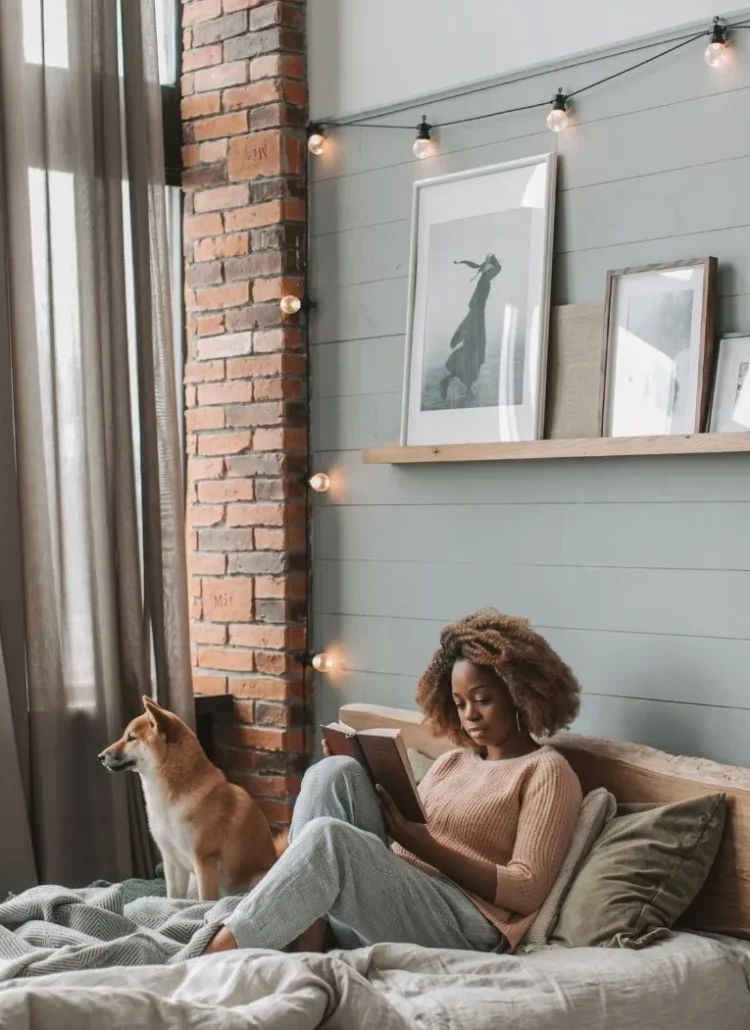 woman sitting on her bed with her dog reading a book