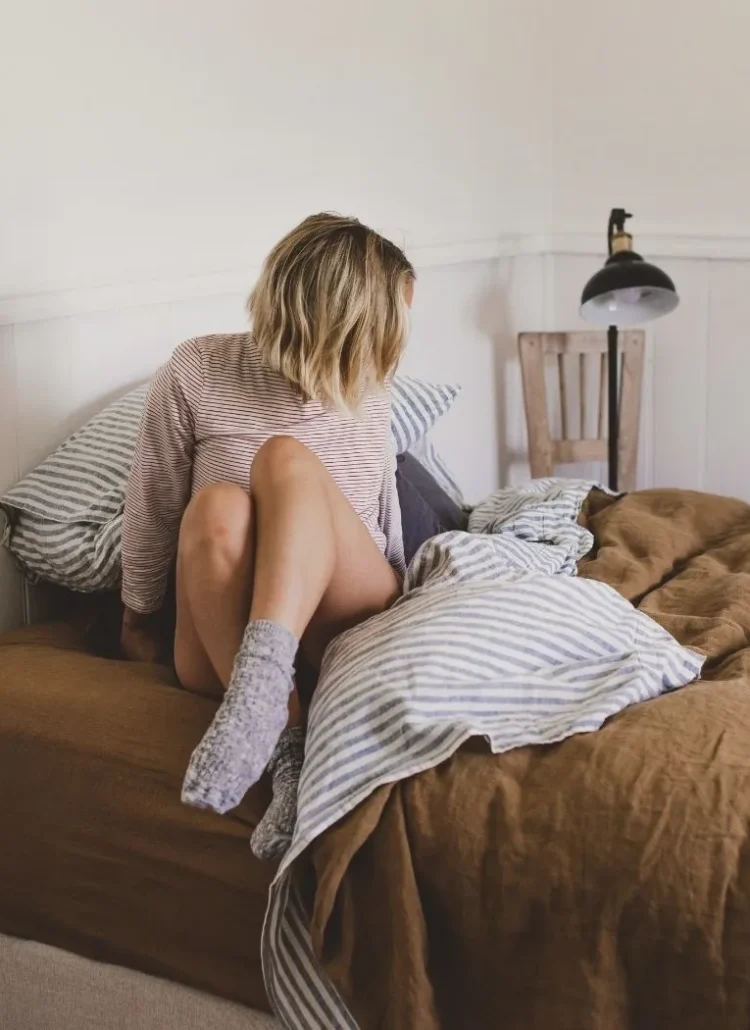 blond hair woman sitting on her bed with face away from camera