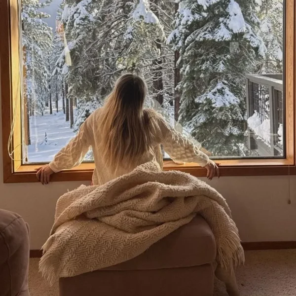 photo of woman in her 30s looking out the window with trees covered in snow